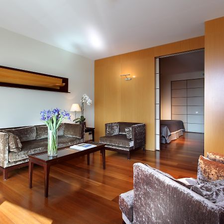 Eurostars Grand Marina Hotel GL Barcelona Exterior foto The photo shows a modern living room with a warm and inviting atmosphere. It features two armchairs and a sofa, all in a plush, dark fabric. A coffee table sits in the center, with a vase of fresh flowers adding a pop of color. The room has hardwood 