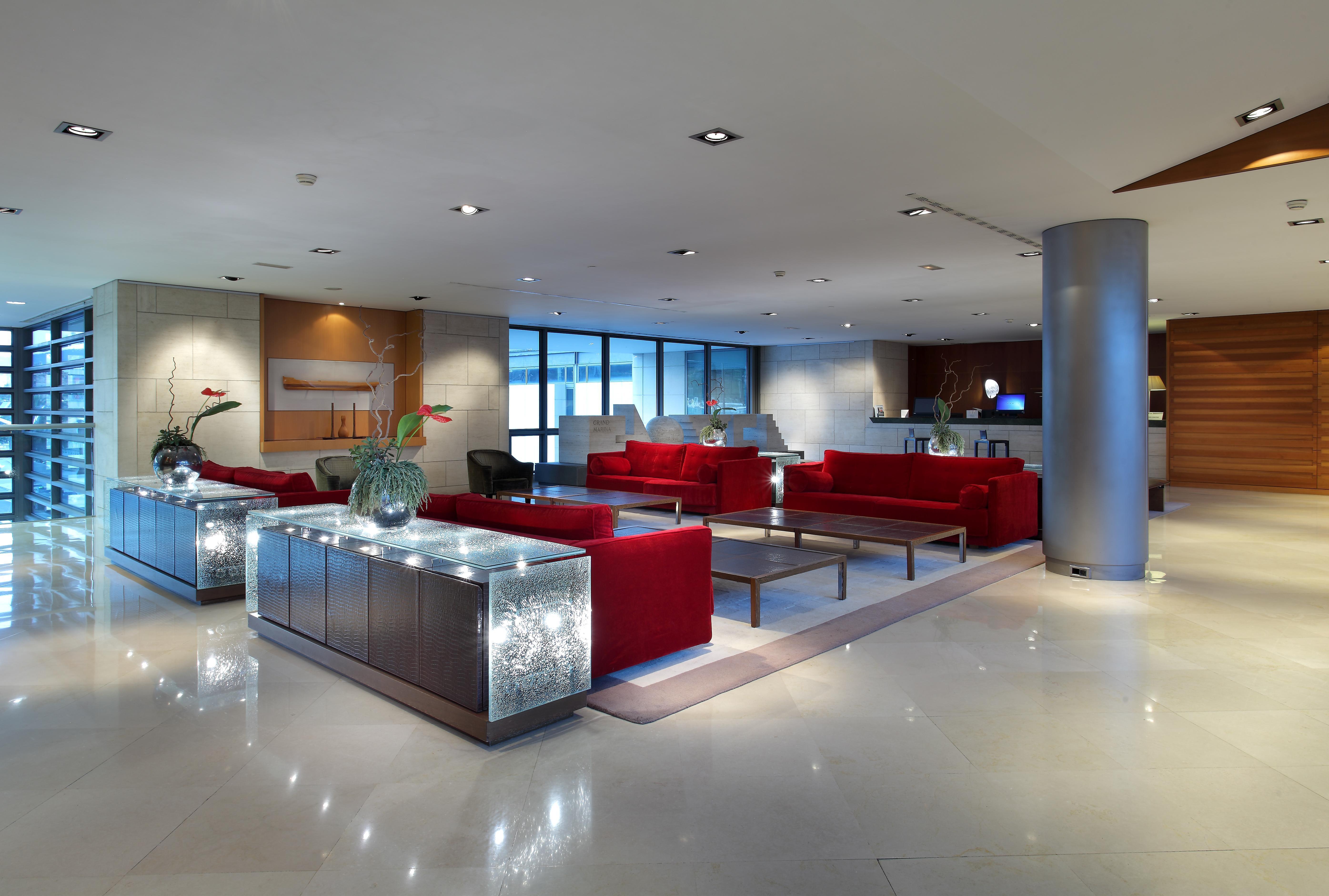 Eurostars Grand Marina Hotel GL Barcelona Exterior foto The photo depicts a modern lobby area, featuring stylish furnishings. There are several red sofas arranged around coffee tables, creating a comfortable seating area. The flooring looks polished and smooth, with a neutral color that complements the fu