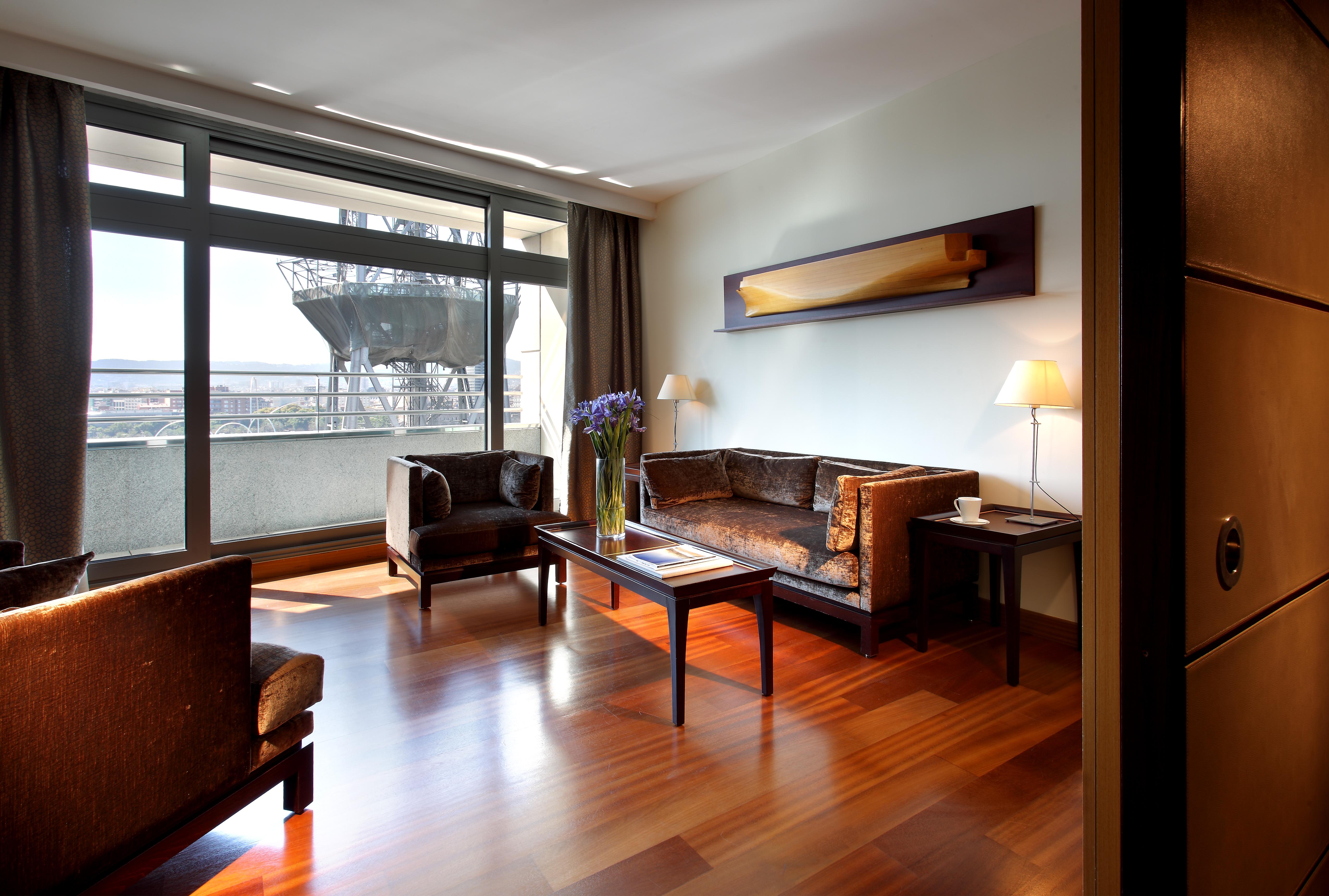 Eurostars Grand Marina Hotel GL Barcelona Exterior foto The photo depicts a modern living room setting. It features a spacious area with large windows allowing natural light to flood in. The room is furnished with two dark chairs and a brown couch, all arranged around a wooden coffee table. A decorative l