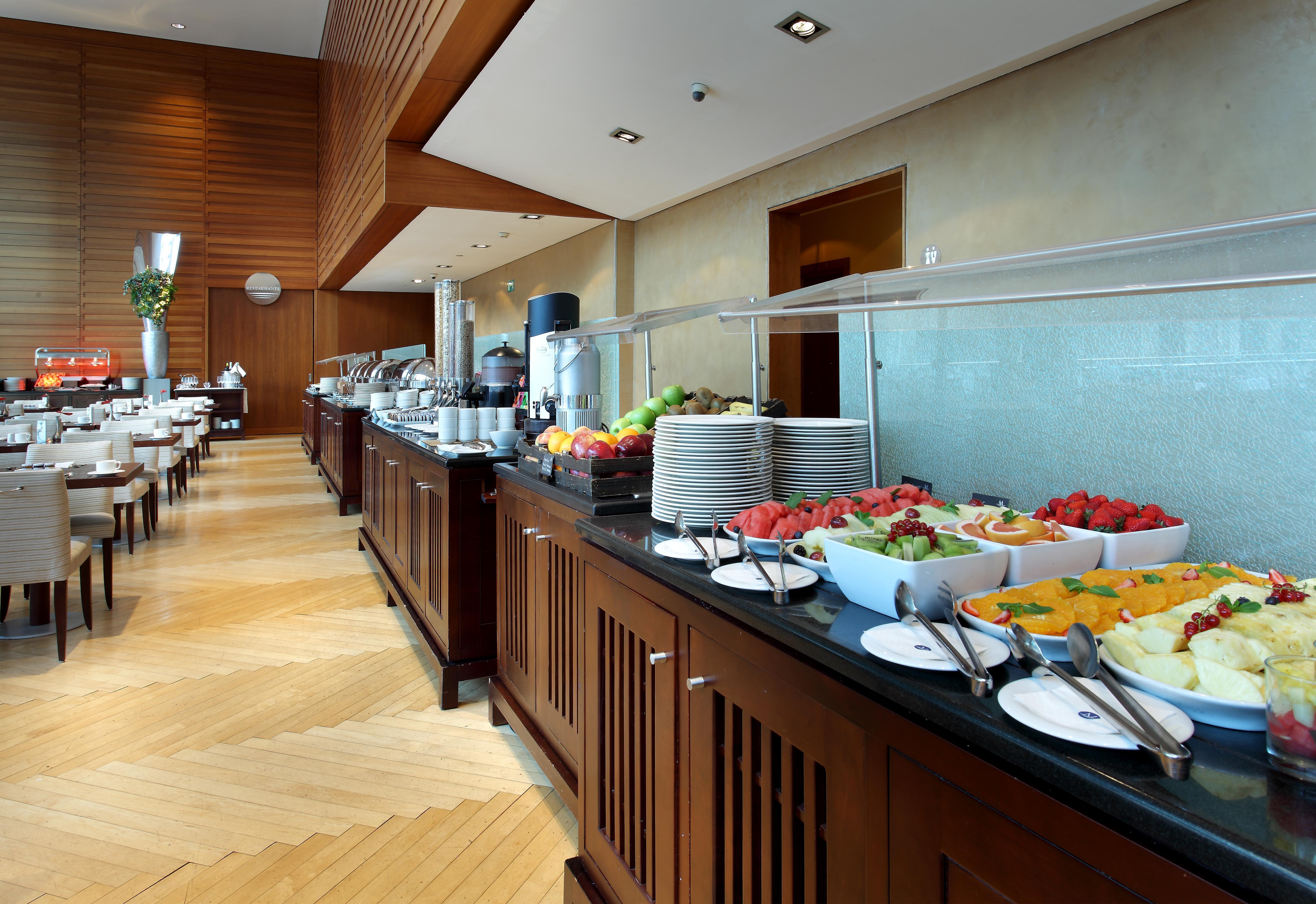 Eurostars Grand Marina Hotel GL Barcelona Exterior foto The photo shows a well-organized buffet setup in a modern dining area. There is a long counter made of wood, displaying a variety of food items. Several bowls filled with fresh fruits, such as melons and strawberries, are prominently placed. In the b
