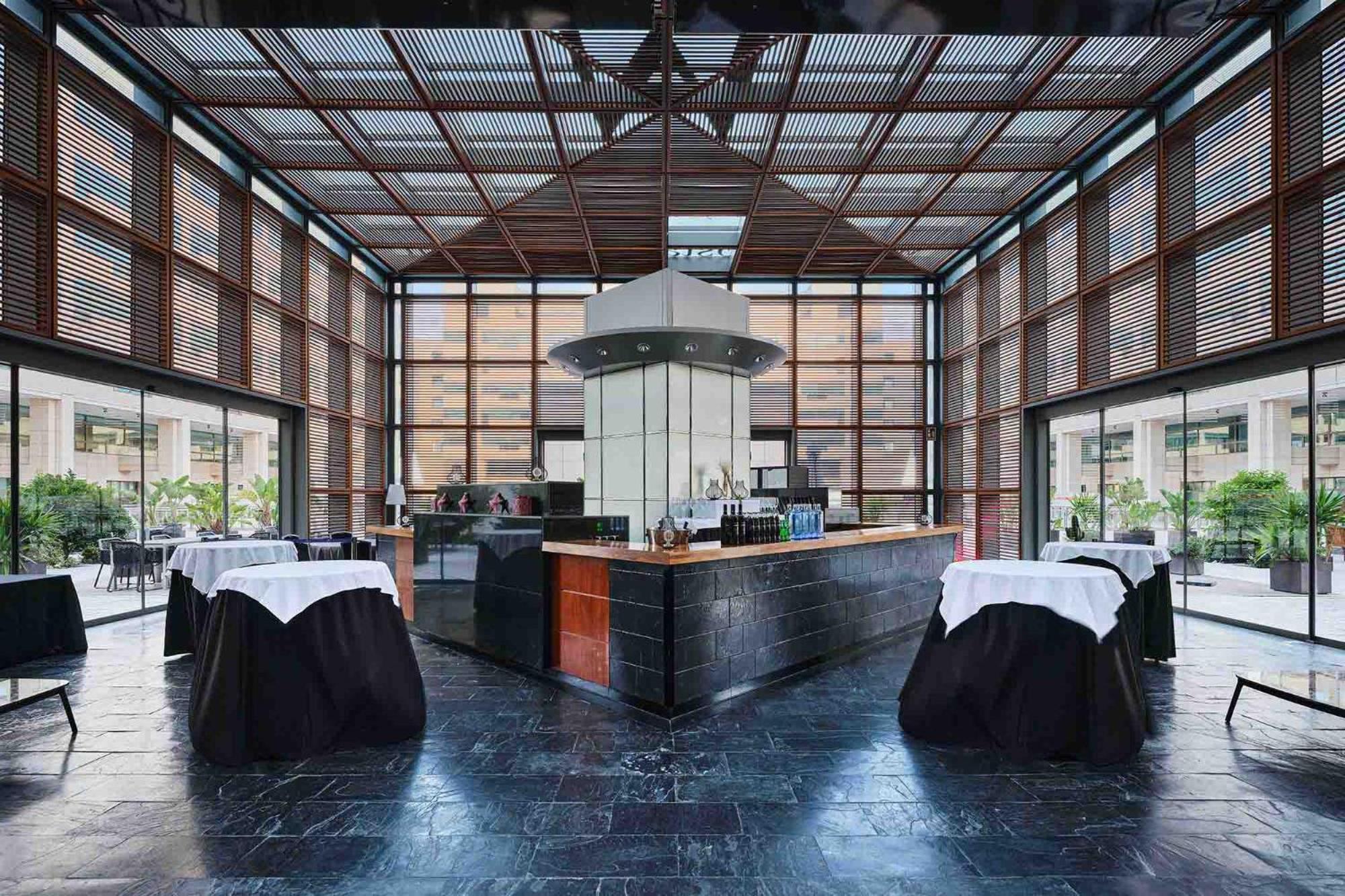Eurostars Grand Marina Hotel GL Barcelona Exterior foto The photo shows the interior of a modern restaurant featuring a sleek bar area. The bar is centrally located and has a metallic structure with a contemporary design. Surrounding the bar are several tables covered with dark cloths and white table runn