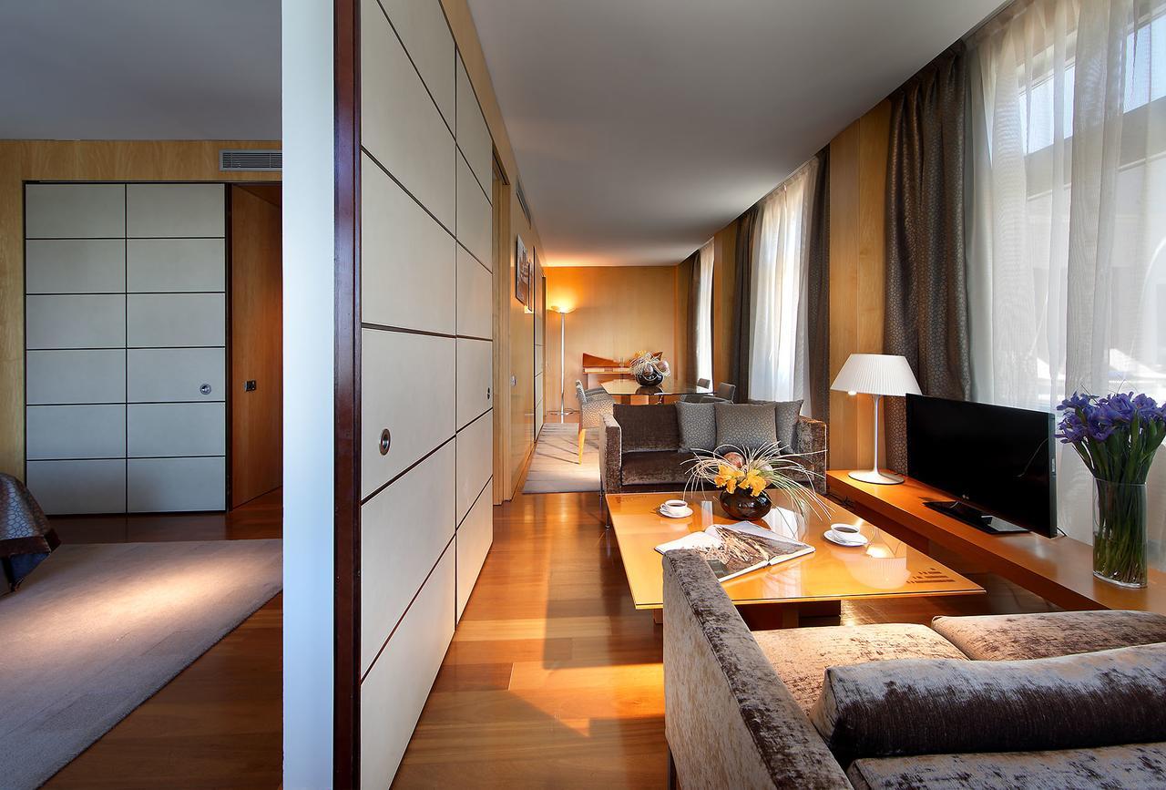 Eurostars Grand Marina Hotel GL Barcelona Exterior foto The photo shows a modern, well-lit interior space, likely a living room or suite. On one side, there are large windows letting in natural light, and the walls are adorned with soft colors. A comfortable seating area features a plush sofa and chairs, 